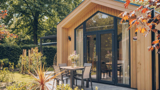 Tiny Lodge met hottub, moderne houten gevel en knus terras, omgeven door groene tuin en bomen.