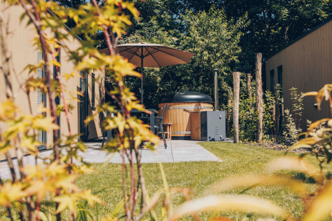 Terraza acogedora con jacuzzi, sombrilla y jardín en Tiny Lodge de Veluwepark de Bosgraaf, Países Bajos.