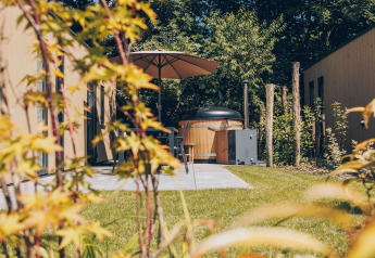 Terrazza accogliente con vasca idromassaggio, ombrellone e giardino al Tiny Lodge di Veluwepark de Bosgraaf.