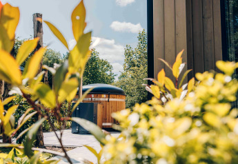 Uitzicht op een tiny lodge met hot tub bij Veluwepark de Bosgraaf in Nederland, omringd door groen.