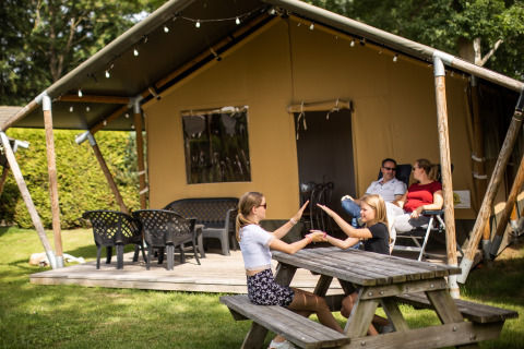 Familia descansando en De Scherpenhof, un parque vacacional en Gelderland, Países Bajos, junto a una tienda.