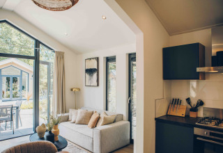 Sala moderna y cocina en una Tiny Lodge en Veluwepark de Bosgraaf, con vista al jardín y terraza exterior.