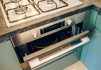 Forno e piano cottura moderni installati nella cucina di una tiny house con mobili verdi e piano scuro.