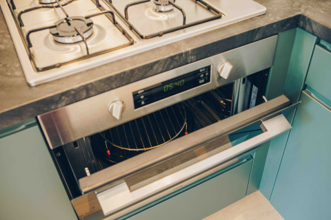 Moderne kookplaat en oven ingebouwd in een tiny house-keuken met groene kasten en donker werkblad.
