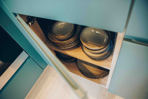 Open kast in een tiny house keuken met borden en kommen netjes gestapeld op houten legplanken.