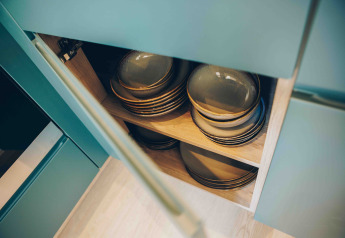 Armadio aperto in una tiny house che mostra piatti e ciotole impilati ordinatamente su mensole in legno.
