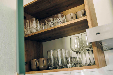Armario abierto en una tiny house con vasos, copas de vino y tazas organizados cuidadosamente en estantes.