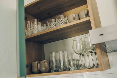 Openkast in een tiny house, toont ordelijk geordende glazen, kopjes en wijnglazen op houten legplanken.