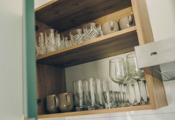 Open cupboard in a tiny house kitchen, displaying neatly arranged mugs, glasses, tumblers, and wine glasses.