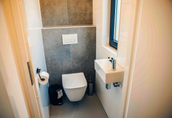 Bagno compatto e moderno con wc sospeso, lavandino piccolo e finestra in una Tiny Lodge al Veluwepark de Bosgraaf.
