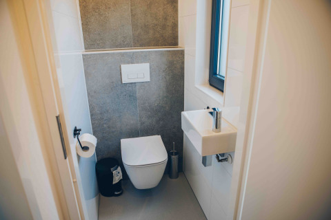 Kleines, modernes Badezimmer mit wandmontierter Toilette, kleinem Waschbecken und Fenster im Tiny House in Veluwepark de Bosgraaf.
