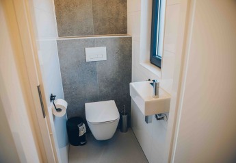 Baño pequeño y moderno con inodoro suspendido, pequeño lavabo y ventana en una Tiny Lodge en Veluwepark de Bosgraaf.