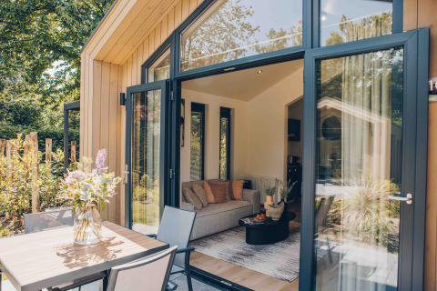 Exterior and interior view of Tiny Lodge with large windows and cozy decor at Veluwepark de Bosgraaf, Netherlands.
