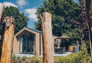 Tiny Lodge with patio seating and hot tub at Veluwepark de Bosgraaf, Netherlands, surrounded by trees.