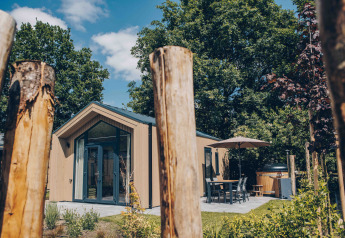 Tiny Lodge med udendørs spiseplads og spabad i Veluwepark de Bosgraaf, Holland, omringet af natur.
