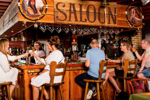 Gezellige sfeer in de Saloon bar van vakantiepark De Scherpenhof, met gasten aan de toog in Gelderland.