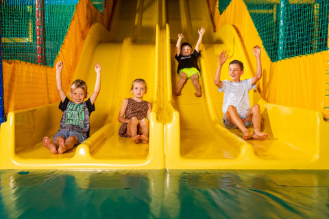 Kinderen genieten van een ritje op gele glijbanen in het overdekt speelparadijs van De Scherpenhof.