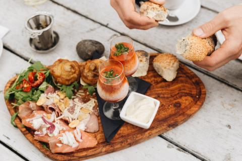 Een houten plank met diverse vleeswaren, salade, broodjes, muffins en twee glazen soep bij Beerze Bulten.