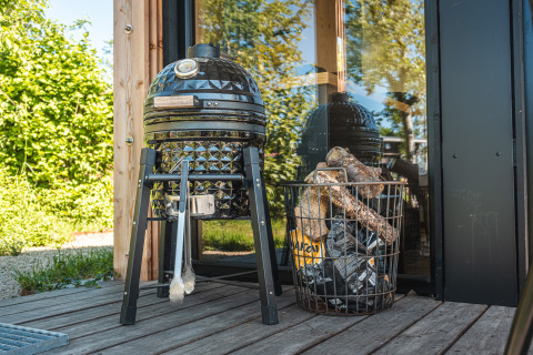 Schwarzer Egg-Barbecue-Grill und Korb mit Holz auf der Terrasse der Tiny house XL Lodge in Holland.
