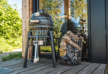 Black egg barbecue grill and firewood basket on wooden deck at Tiny house XL lodge in the Netherlands.