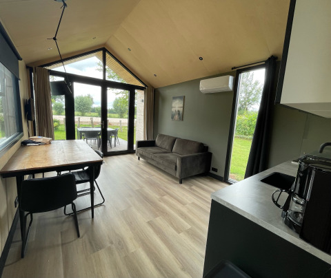 Interno luminoso di Tiny House XL con divano, tavolo e cucina a Holiday park Eigen Wijze, Paesi Bassi.