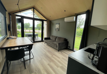 Bright interior of Tiny House XL with sofa, table, and kitchen at Holiday park Eigen Wijze, Netherlands.