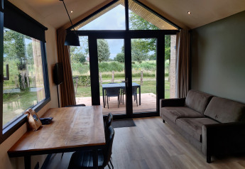 Interior view of a cozy lodge with sofa, dining table, and large windows overlooking a green landscape.
