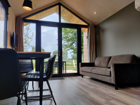 Wohnbereich im Tiny House XL mit großen Fenstern, Sofa und Tisch im Holidaypark Eigen Wijze, Niederlande.