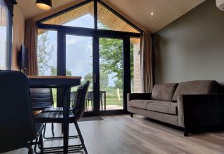 Living area in Tiny House XL with large windows, sofa, and table at Holiday park Eigen Wijze, Netherlands.