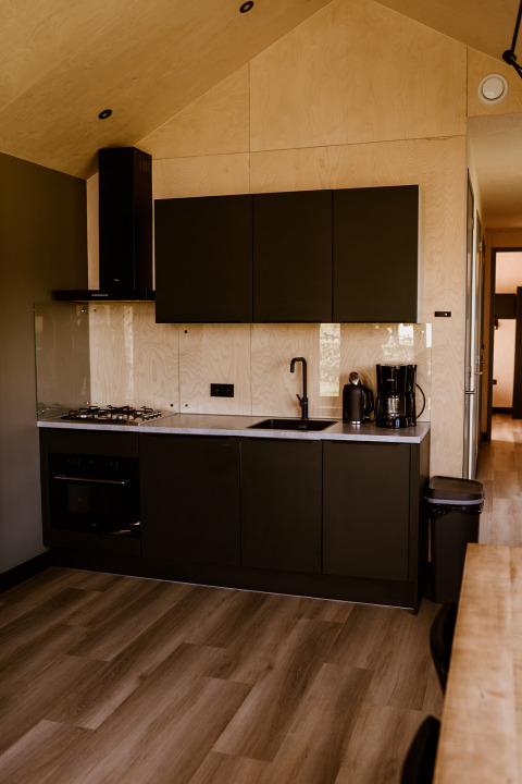 Modern black kitchen in Tiny House XL with wood accents at Holiday park Eigen Wijze, Netherlands.