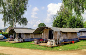 Image of modern tents with wooden decks and outdoor furniture at a lodge campsite surrounded by trees.