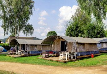Afbeelding van moderne tenten met houten terrassen en tuinmeubilair op een lodgecamping met veel groen.
