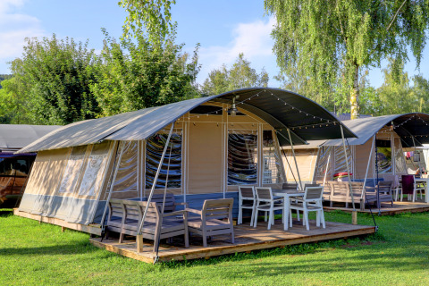 Billede af moderne telt-lodges med terrasse og havemøbler, omgivet af grønne træer og græsplæne.