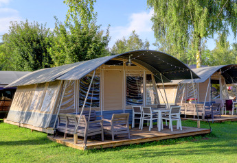 Photo of modern tent lodges with shaded decks and outdoor seating, surrounded by lush greenery and trees.