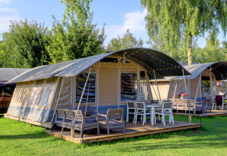 Foto di moderni lodge-tenda con terrazza e mobili da esterno, circondati da prato e alberi verdi.