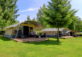 Photo of modern tents with wooden decks and lounge chairs at a scenic, green lodge surrounded by trees.