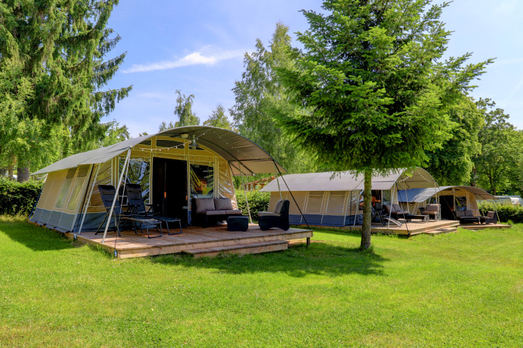 Photo of modern tents with wooden decks and lounge chairs at a scenic, green lodge surrounded by trees.