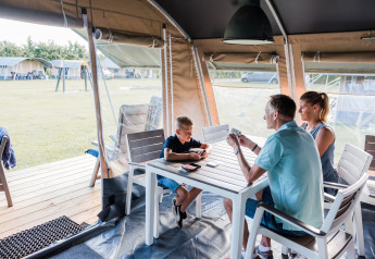 Een gezin speelt gezellig een kaartspel aan tafel in een comfortabele lodgetent op de camping.