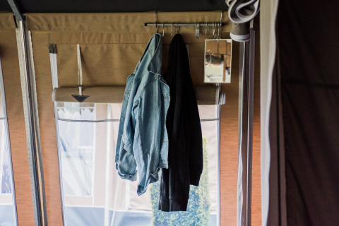 Interno di un lodge con una giacca di jeans e un cappotto scuro appesi, e uno specchio piccolo al muro.