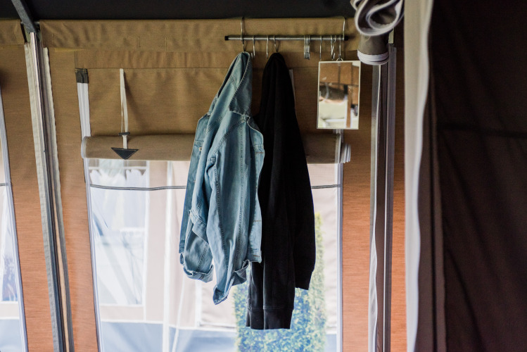Intérieur d’un lodge avec une veste en jean, un manteau sombre suspendus et un petit miroir au mur.