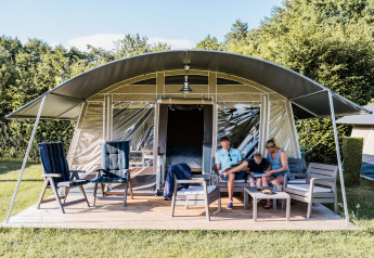 Una famiglia si rilassa davanti a un lodge moderno con tenda, seduta su poltrone all'aperto e godendosi il sole.