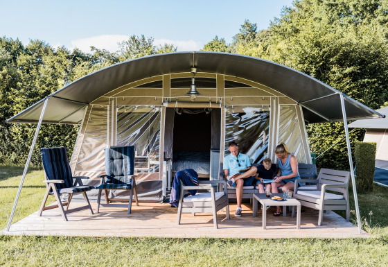 Een gezin zit en ontspant zich buiten voor een moderne tentlodge, omringd door stoelen en een tuintafel.