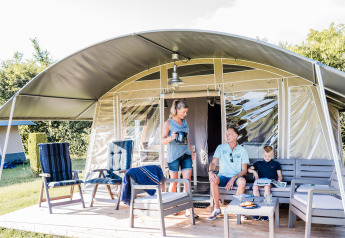 Gezin ontspant op het terras van een lodge met comfortabele stoelen en uitzicht op de groene natuur.