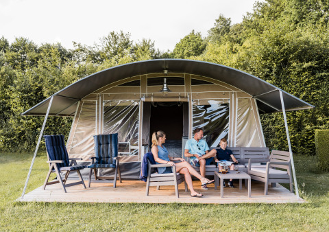 Famille assise sur la terrasse d’un lodge moderne avec mobilier de jardin, entourée de verdure abondante.