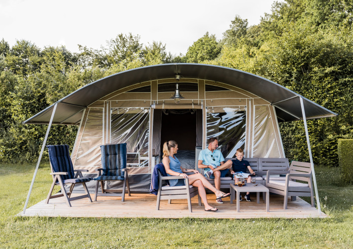 Family relaxing on the terrace of a modern lodge with outdoor furniture, surrounded by lush greenery.