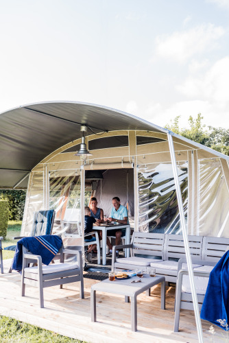 Dos personas disfrutan de una comida juntas en un lodge elegante con muebles modernos y terraza de madera.