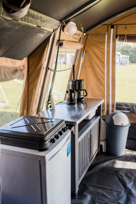 Interior view of a lodge kitchen with coffee maker, stove, cabinet, and trash bin inside the tent.