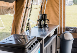 Vue intérieure d'une cuisine de lodge avec cafetière, cuisinière, armoire et poubelle dans la tente.