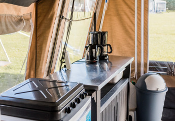 Interior view of a lodge kitchen with coffee maker, stove, cabinet, and trash bin inside the tent.