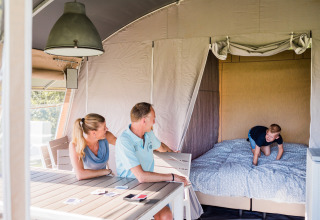 Una familia disfruta en una moderna cabaña; los padres están sentados a la mesa y un niño juega en la cama.